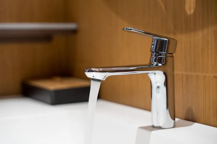Chrome faucet with water running into a white sink, against a wood-paneled wall.
