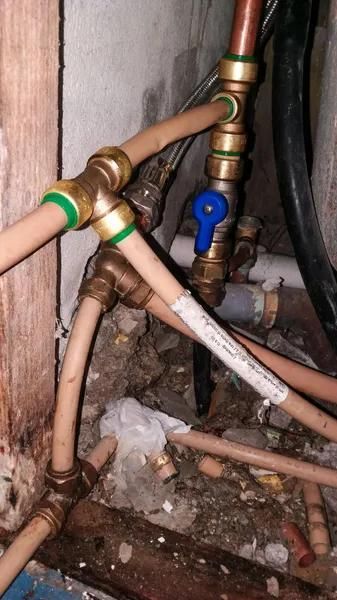 Copper pipes and PEX tubing joined with brass fittings, with a blue valve in a corner.