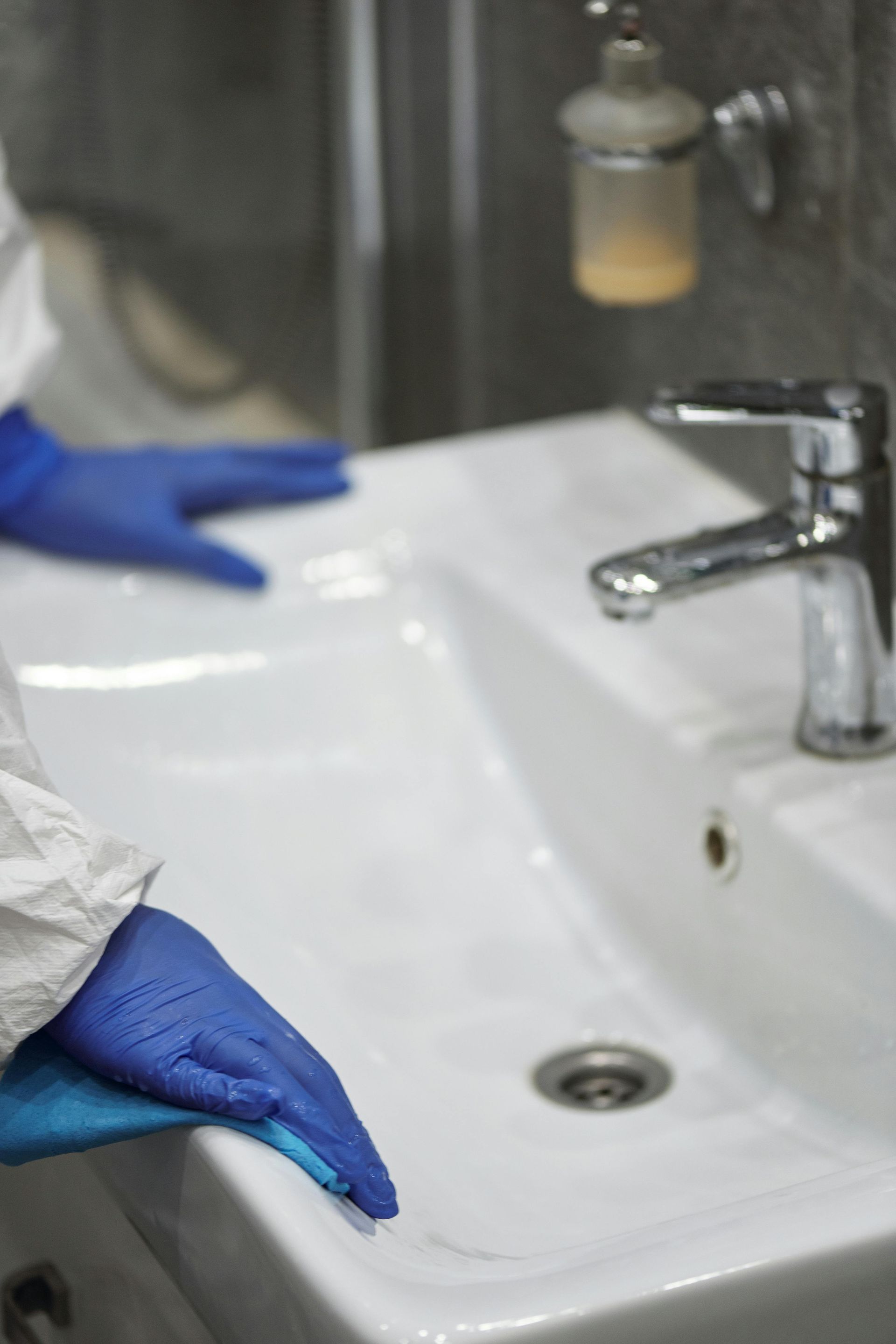 Person in blue jumpsuit working on a faucet in a kitchen.