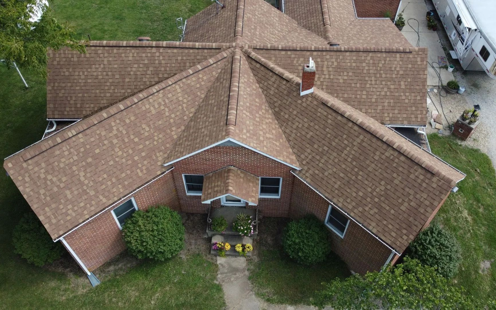Aerial view of a tan-roofed brick house with a central gable and small front garden