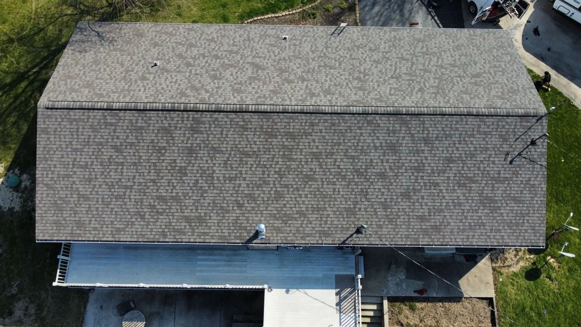 Aerial view of a gray shingled house roof with a blue tarp-covered section and nearby deck.