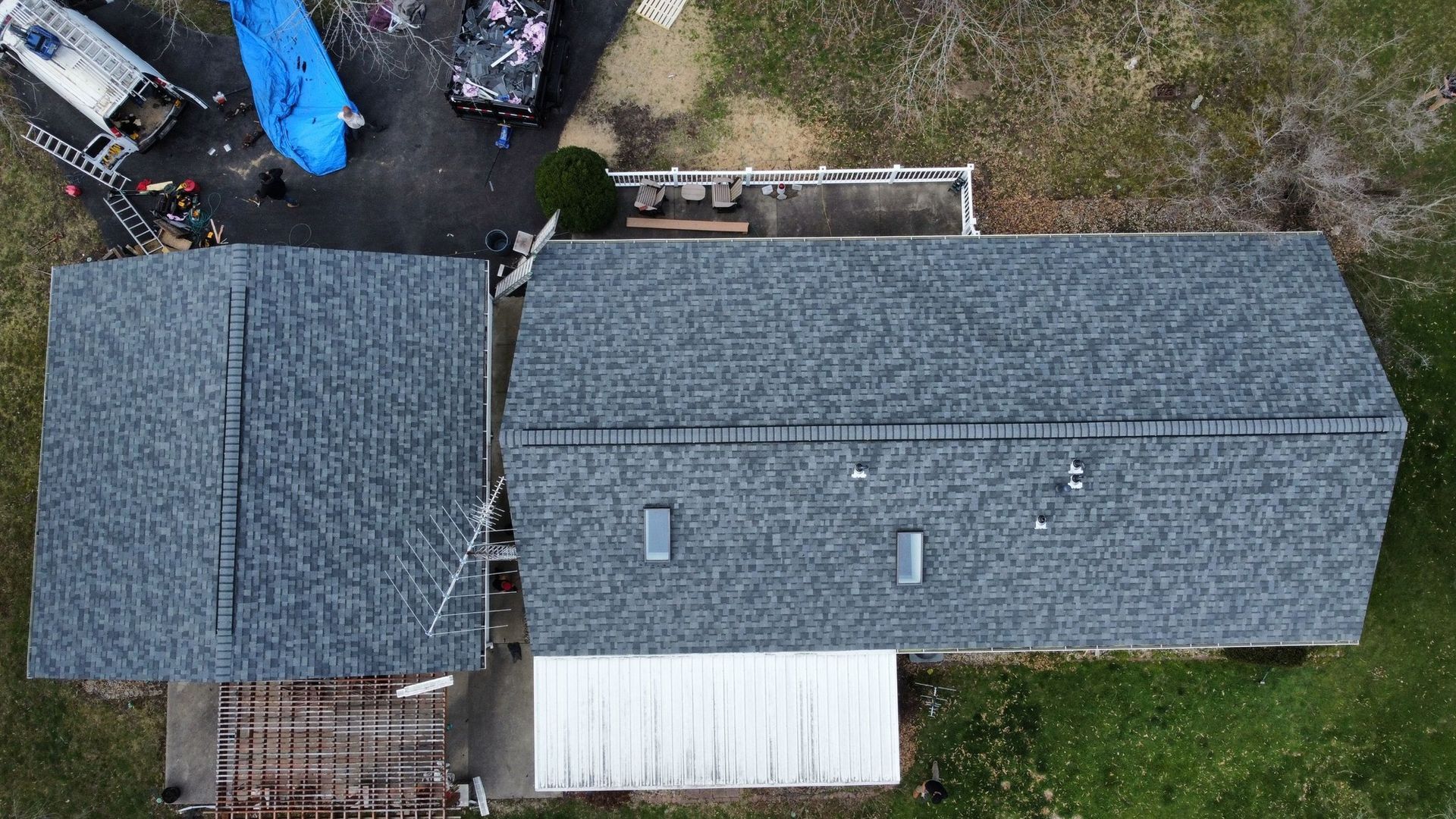 An aerial view of a house roof featuring gray shingles, two skylights, and a white covered patio area.
