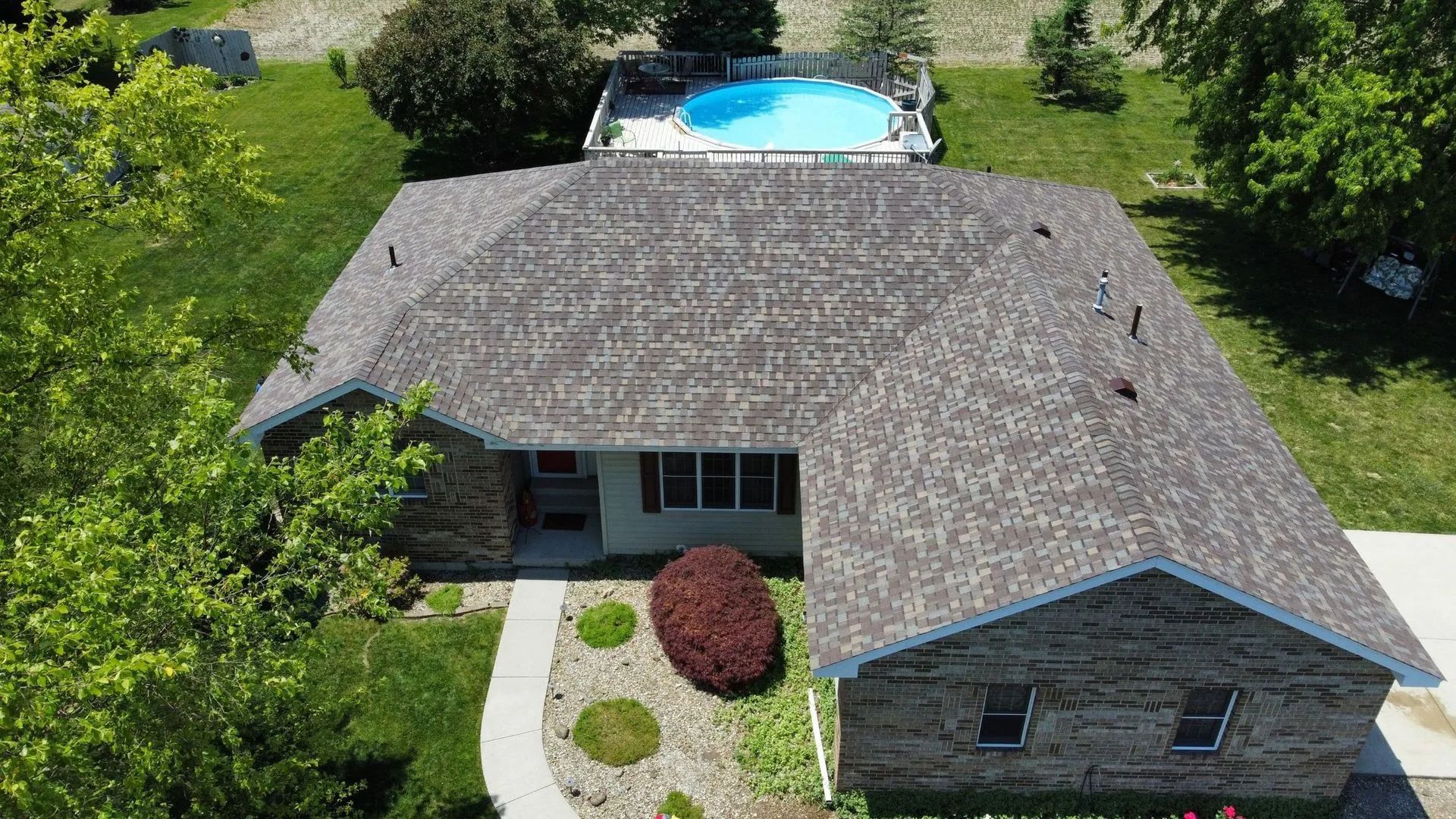 Aerial view of a gray-roofed house with a backyard pool and landscaped front yard.
