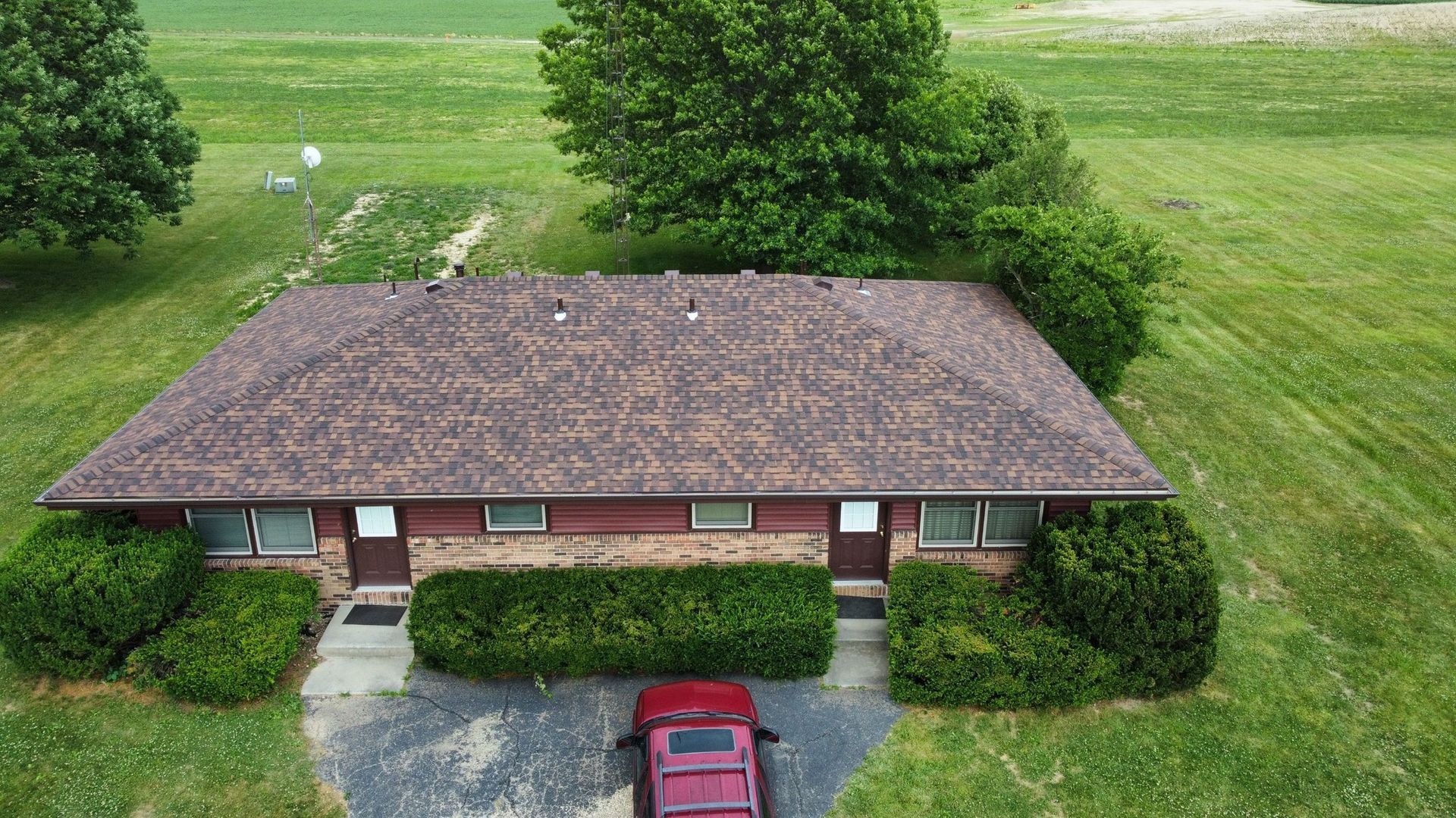 An aerial view of a single-story duplex with a brown roof and a brick facade, surrounded by green lawns and trees.