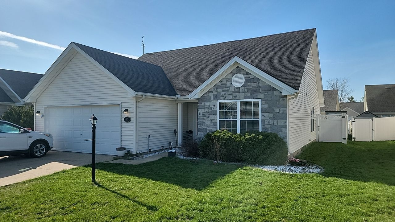 A single-story suburban house with white siding, a stone facade, and a grey shingled roof under a clear blue sky.