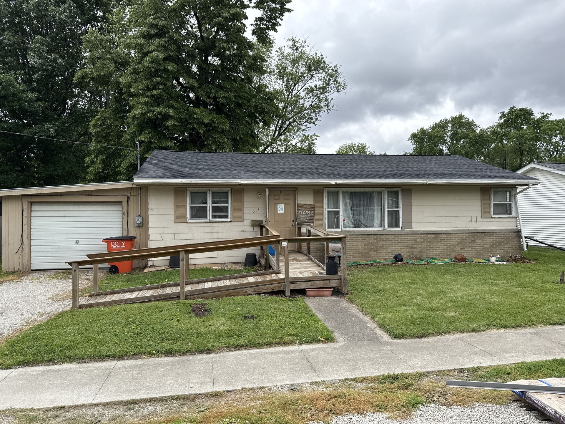 A single-story, light-colored ranch house with a wooden wheelchair ramp leading to the front door and an attached garage.
