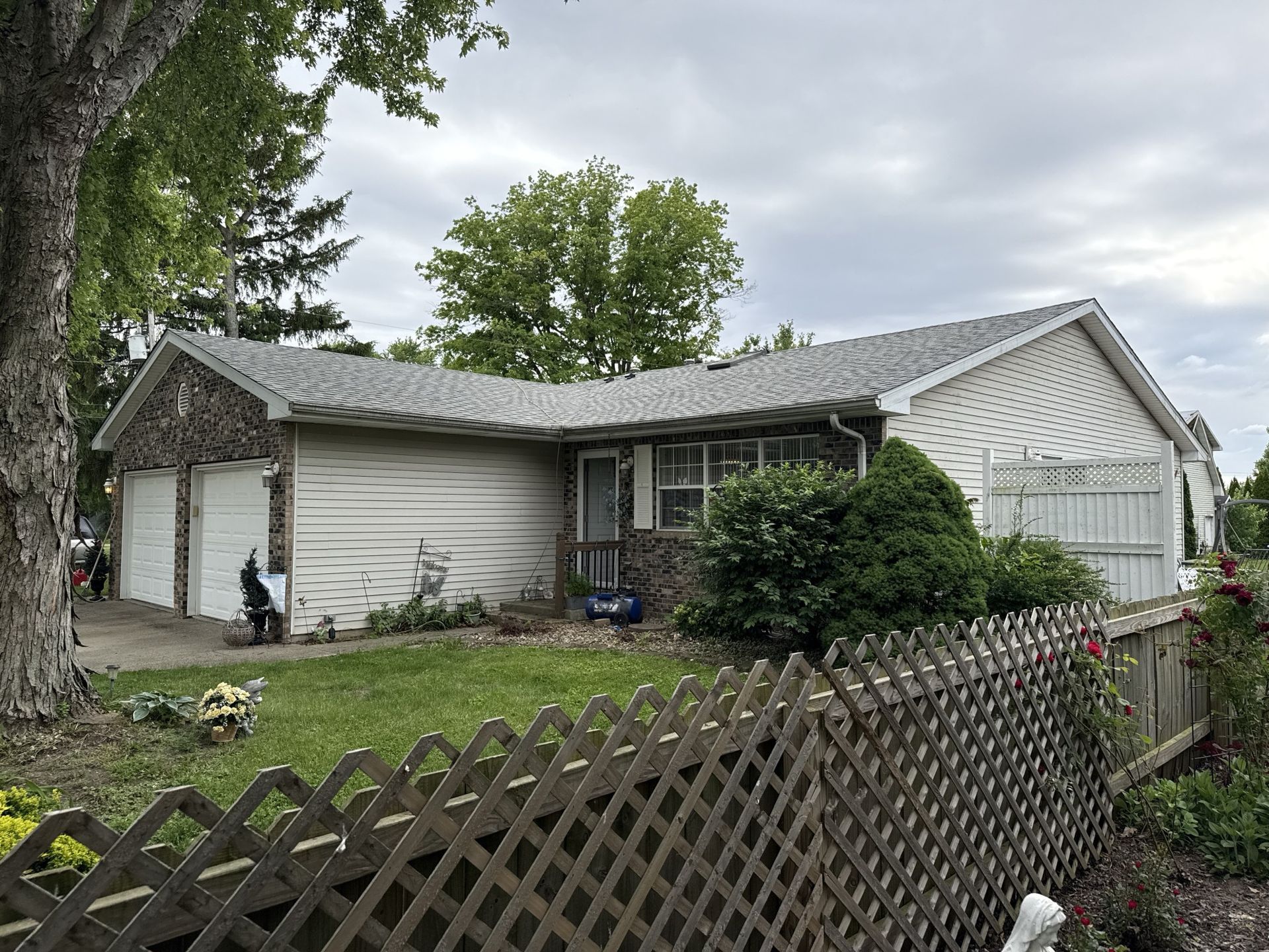 A one-story suburban home with a two-car garage, light siding, a stone facade, and a lattice fence in the front yard.