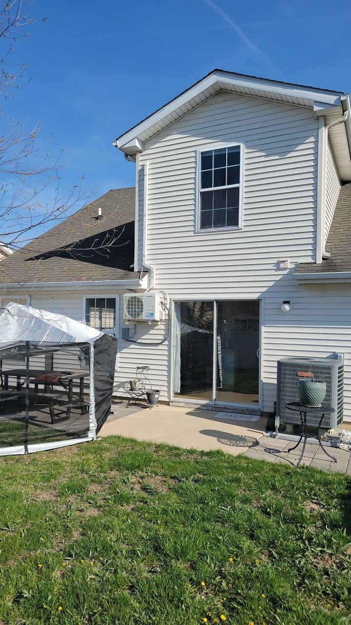 Backyard view of a two-story house with white siding, a sliding door, an outdoor unit, and a screened-in canopy tent.