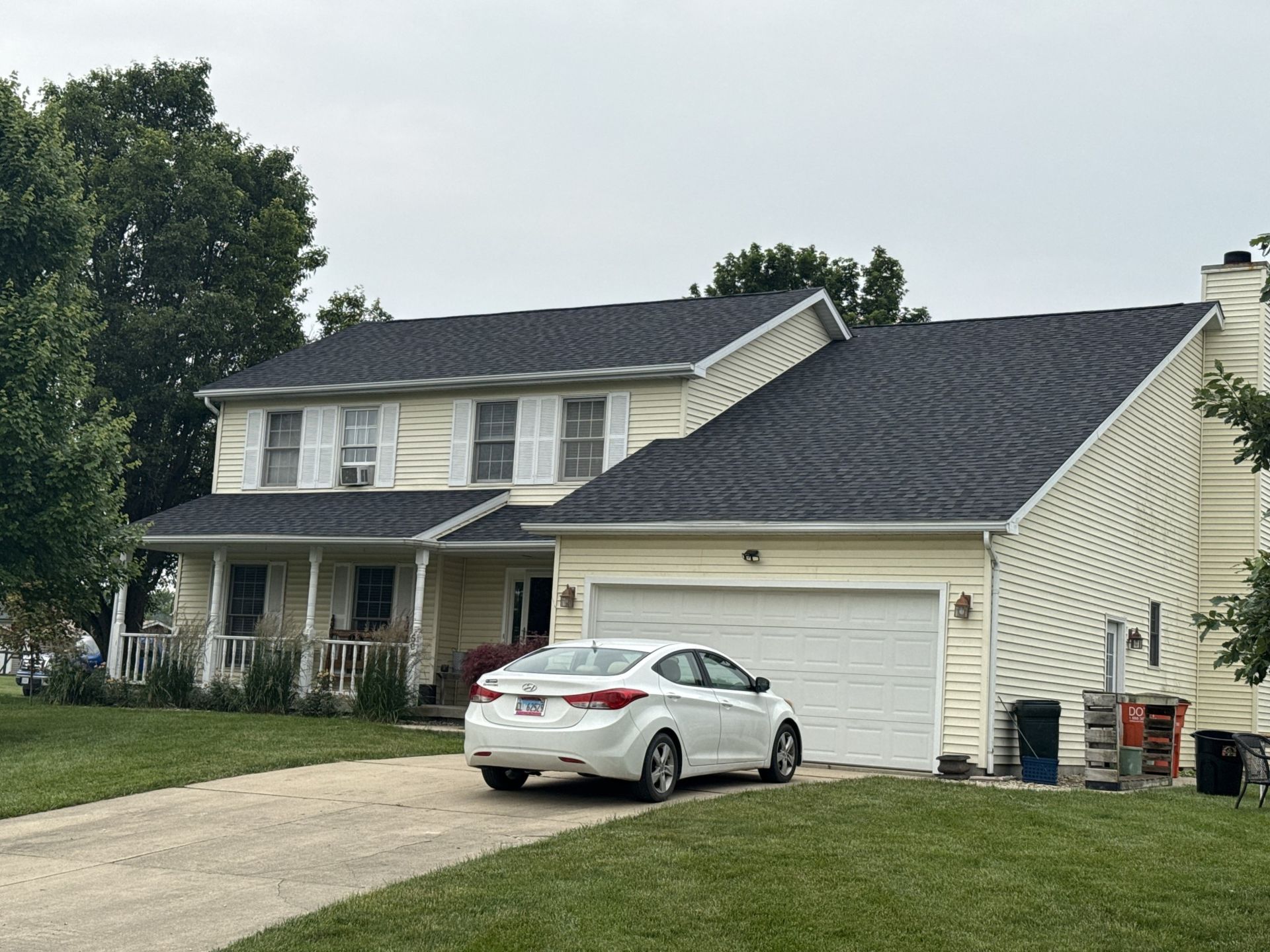 A two-story, yellow-sided house with a dark roof and a white car parked in the driveway.