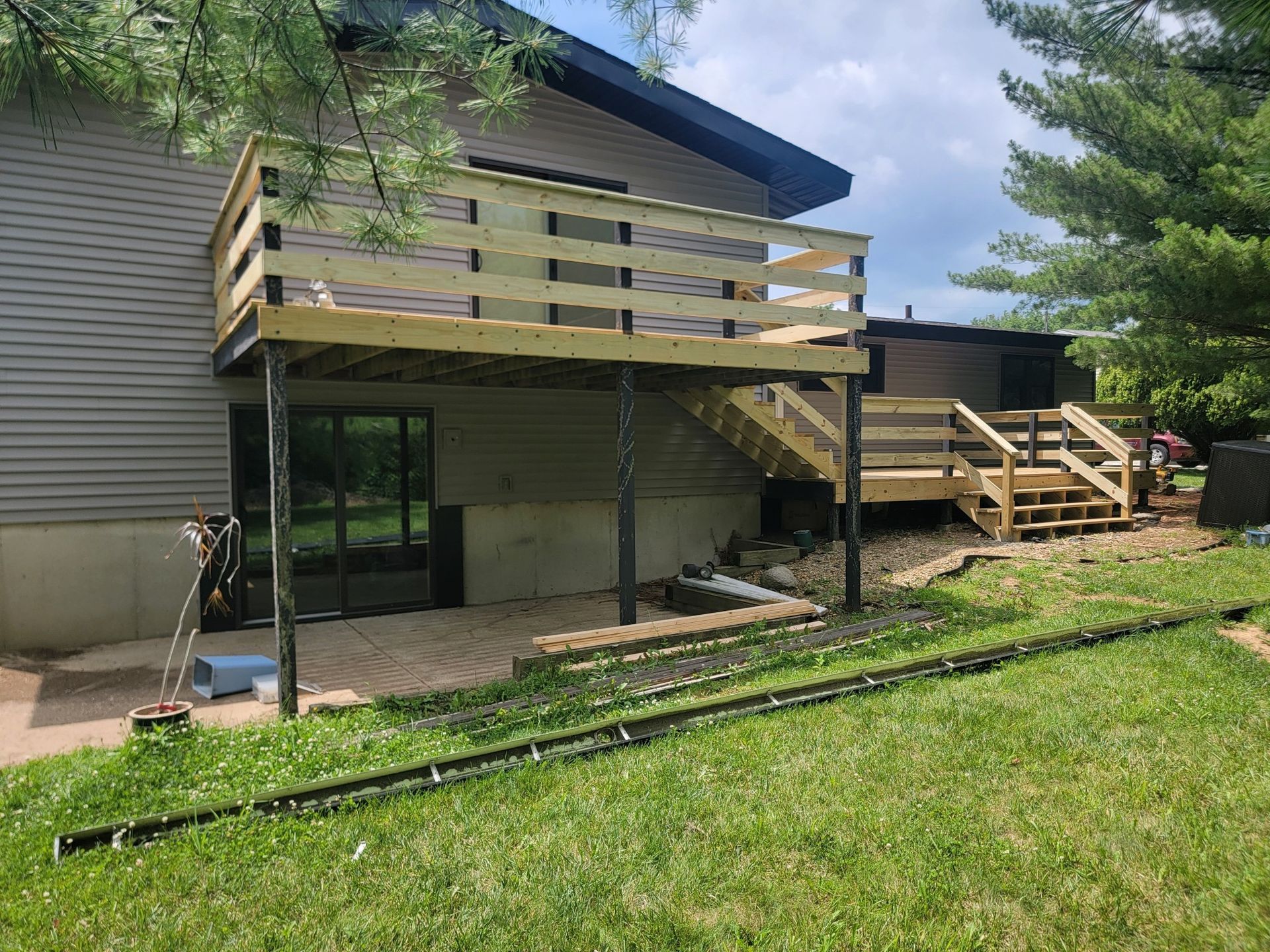 A two-level wooden deck attached to the back of a house, featuring stairs leading down to a stone patio and grassy lawn.