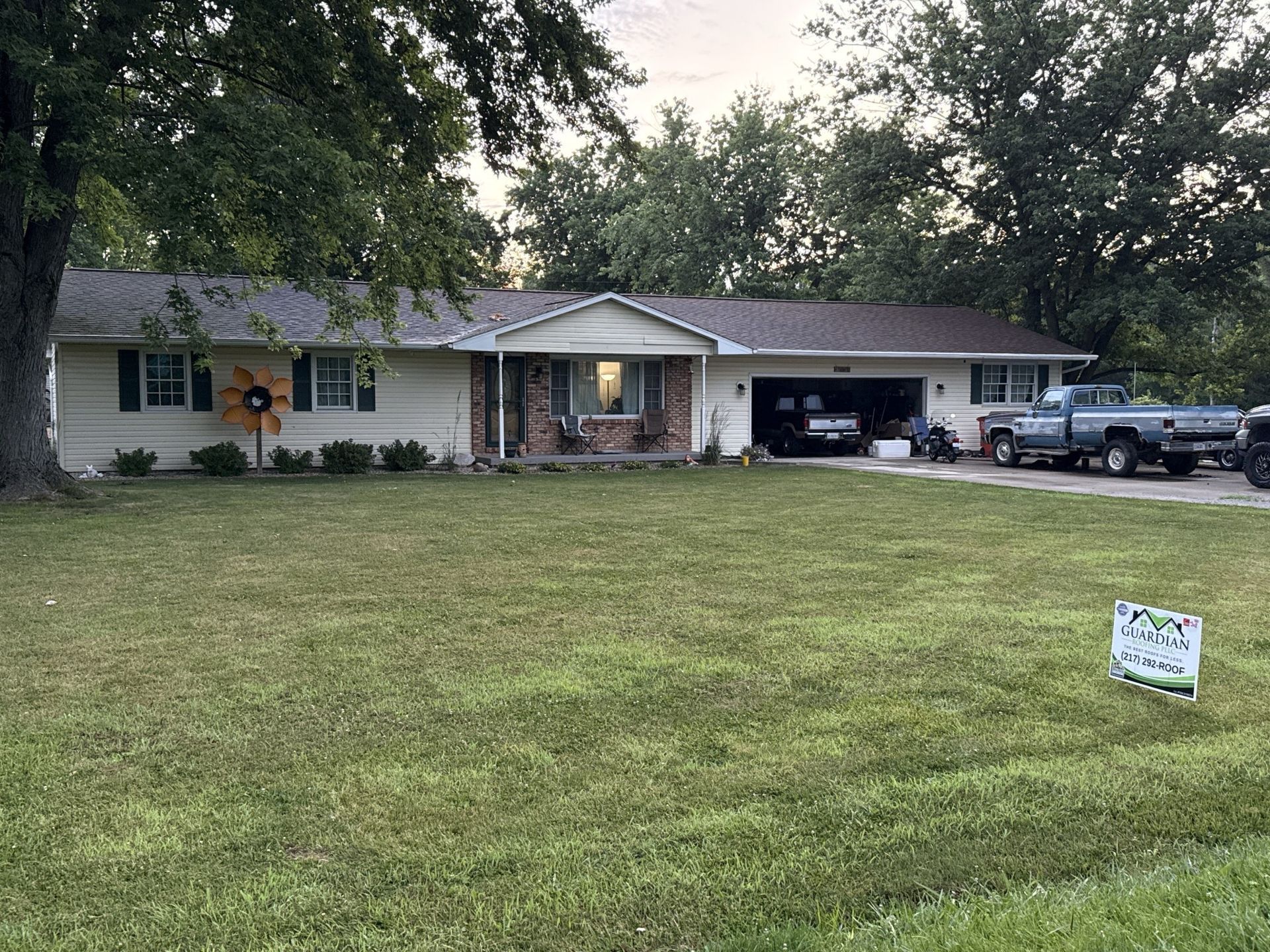 A single-story, light-colored ranch house with a front-facing gable, large lawn, and a pickup truck parked in the driveway.