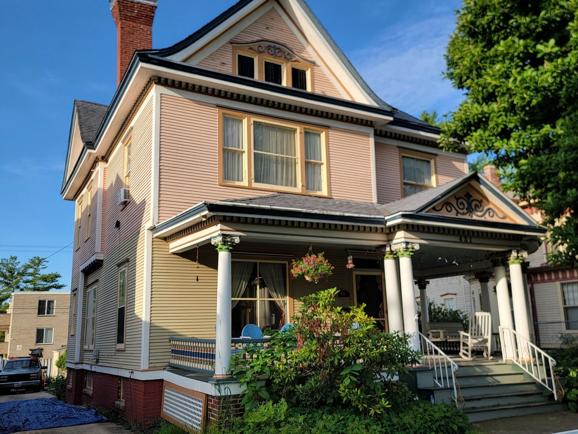 A historic two-story house with pink and cream siding, a brick foundation, a front porch with pillars, and a metal roof.