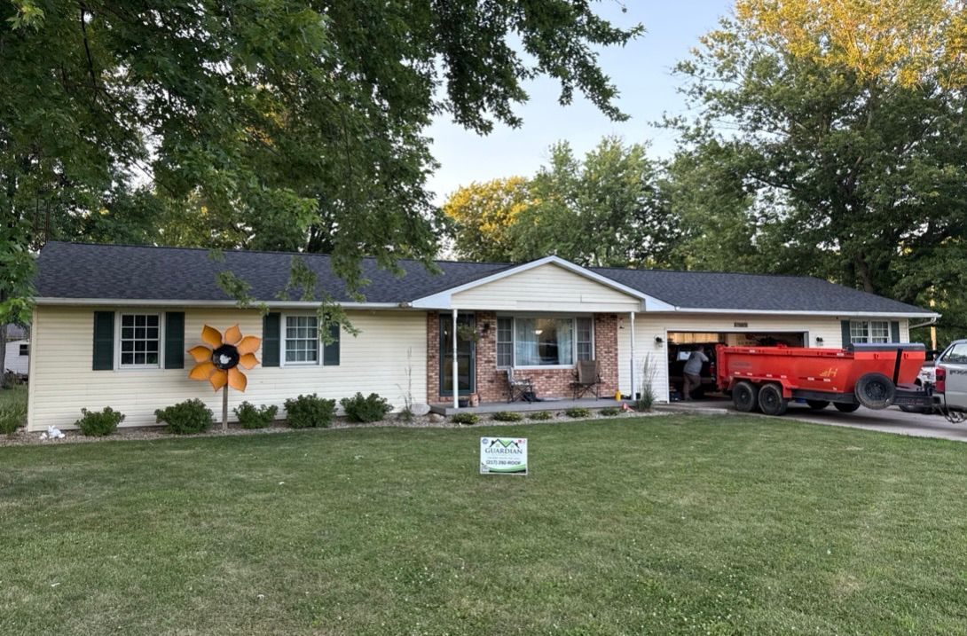 Single-story beige ranch house with a dark shingled roof, a front lawn, and a red trailer parked in the open garage.