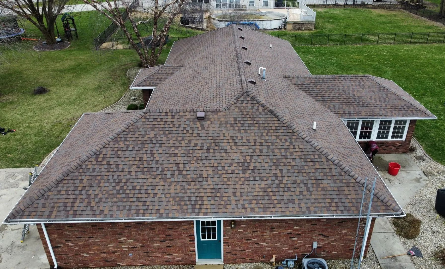 Aerial view of a brown shingle roof on a brick house with a small porch and green yard around it