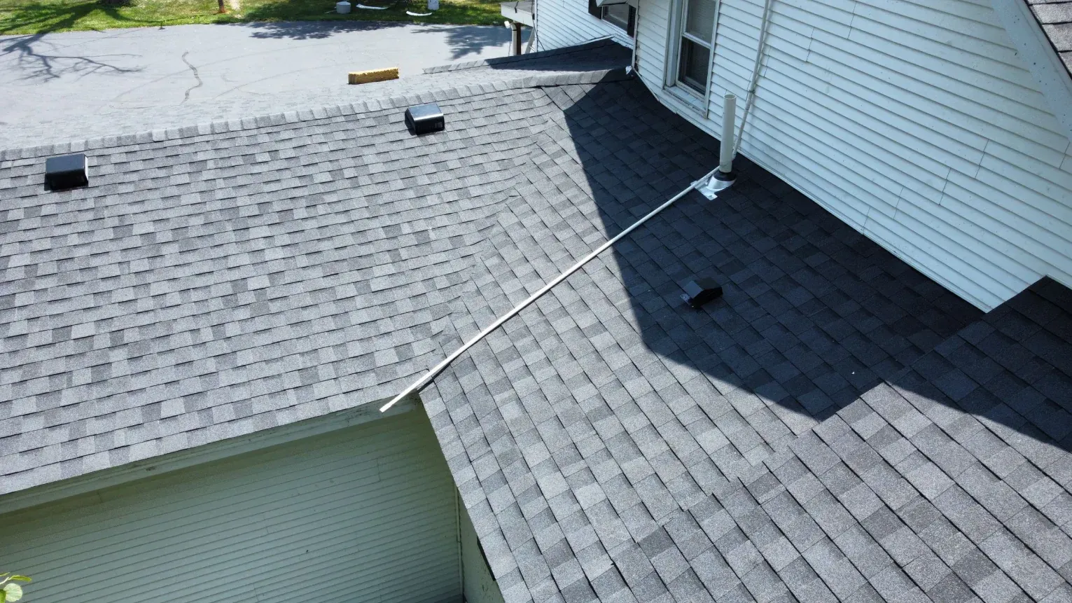 High-angle view of a residential shingled roof with two different gray color patterns and a white pipe vent.