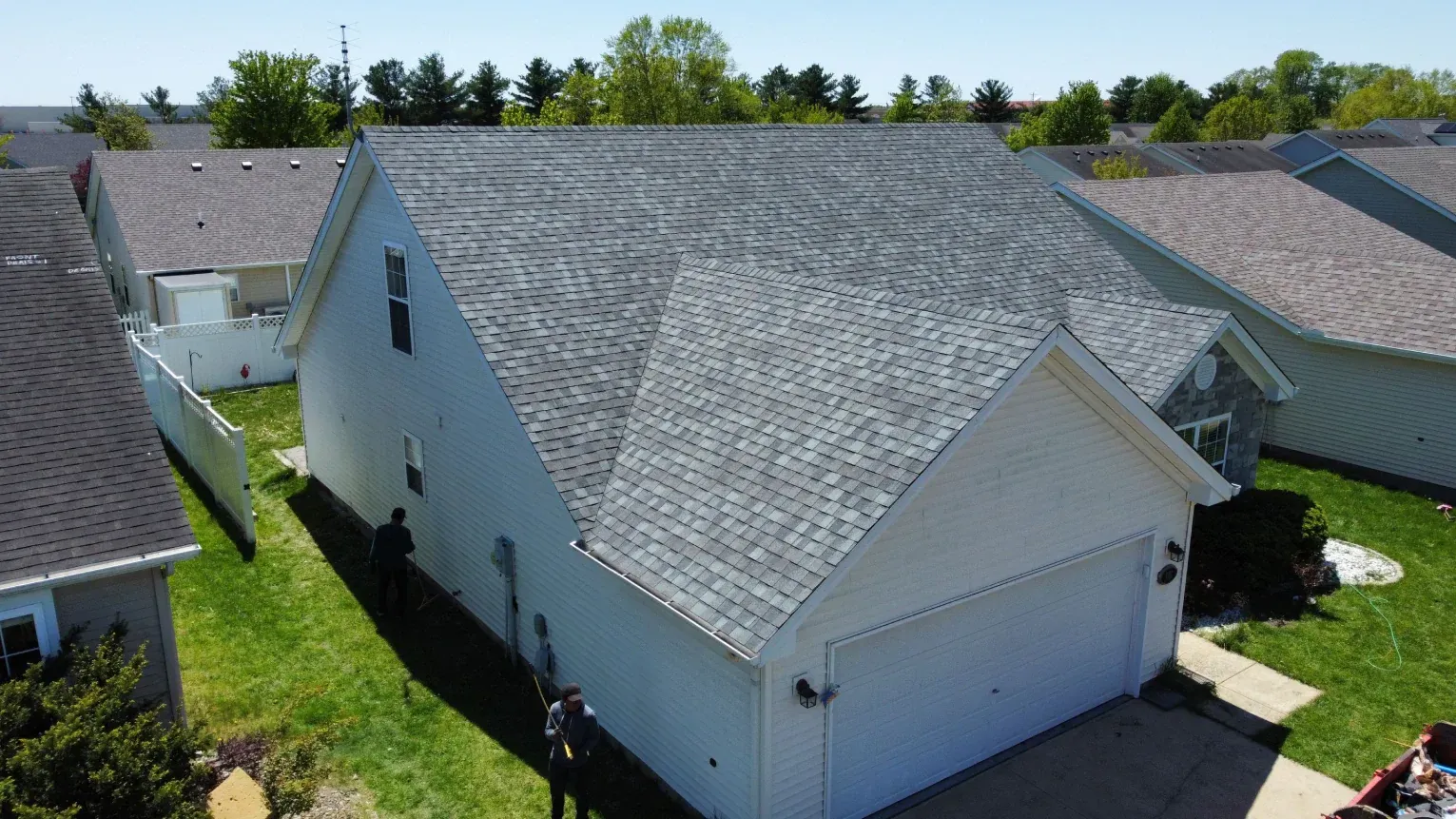 An aerial view of a single-story suburban house with a gray shingled roof, white siding, and an attached two-car garage.