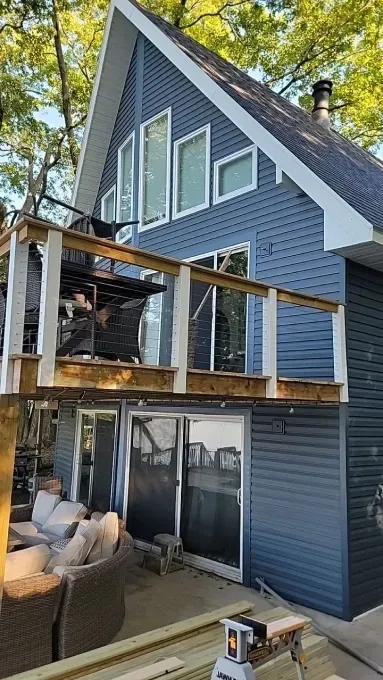 A two-story blue A-frame house with a raised wooden deck and sliding glass doors, nestled among green trees.