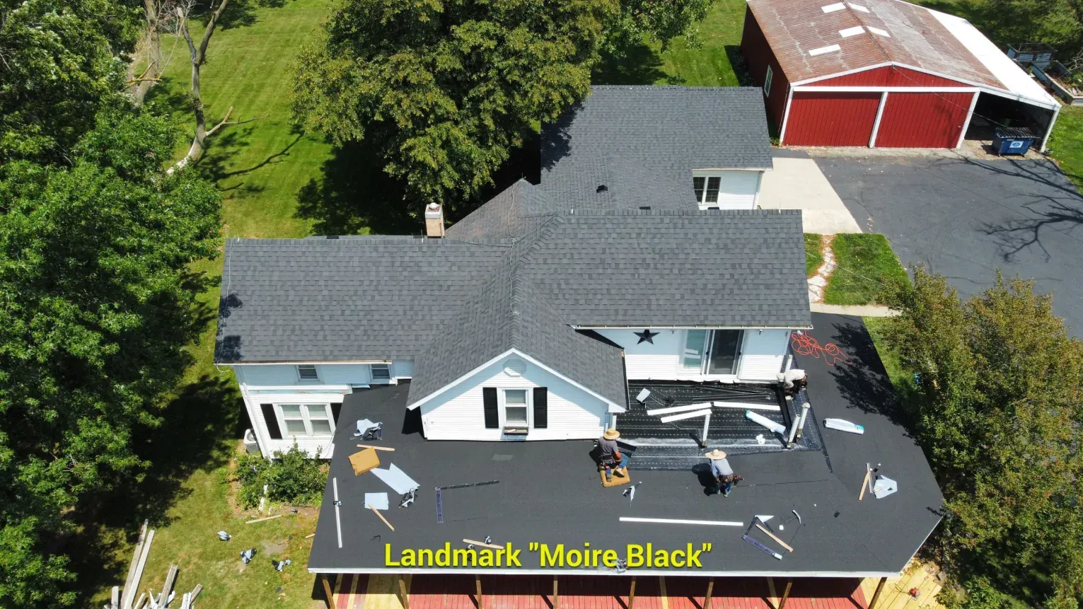 Aerial view of a white house with a newly installed Moire Black roof and an adjacent red garage.