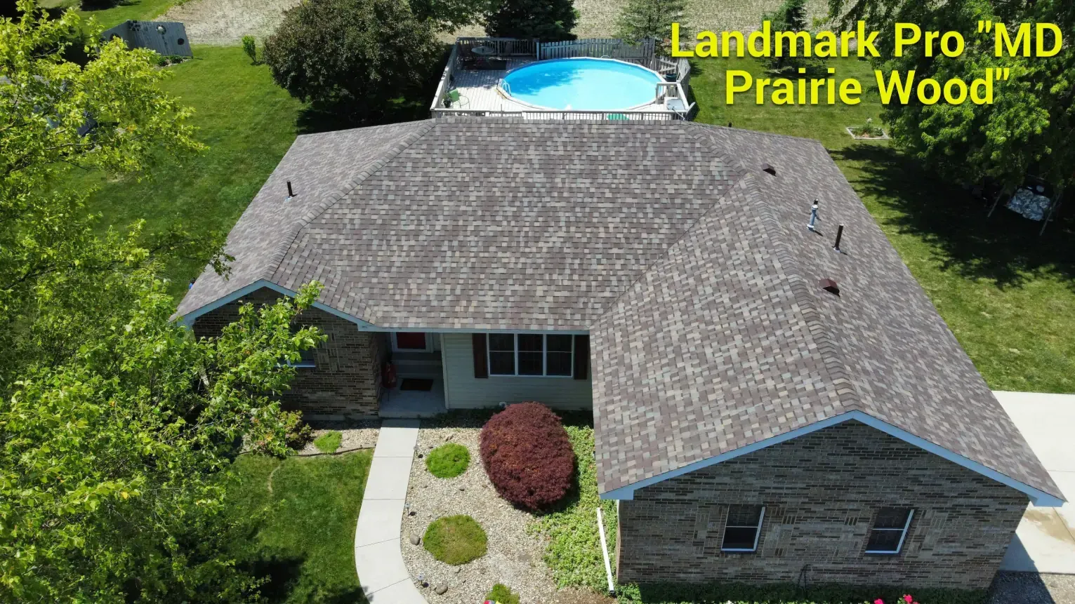 Aerial view of a house with a Landmark Pro MD Prairie Wood shingled roof, next to a swimming pool.