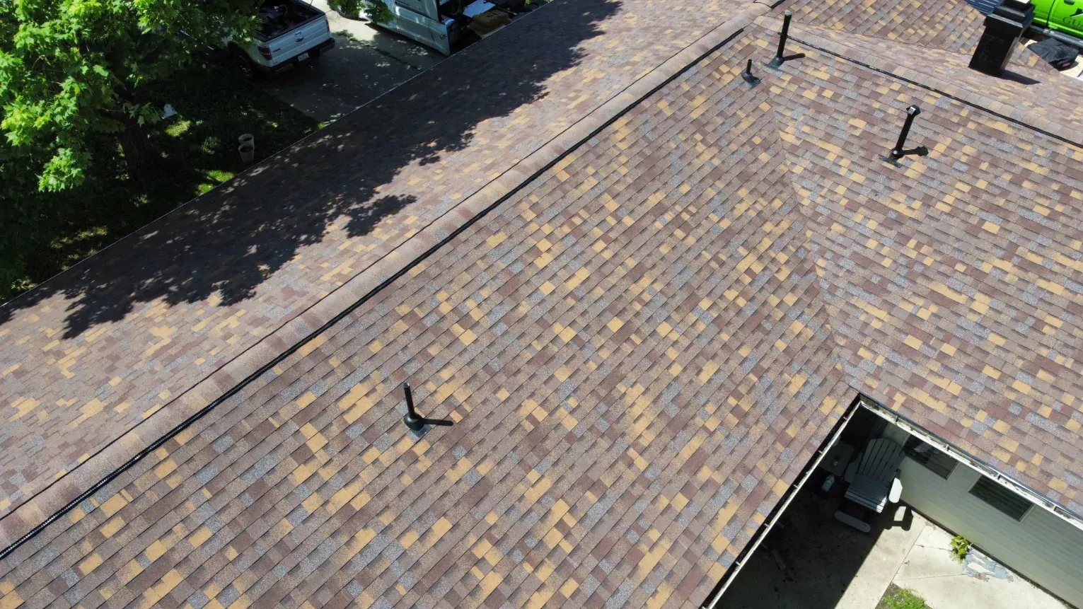 Aerial view of an L-shaped residential roof with brown and tan architectural shingles and several dark plumbing vents.