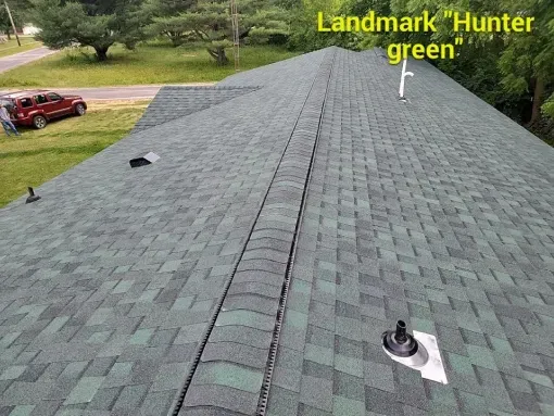 An overhead view of a roof covered in Landmark Hunter Green asphalt shingles, with a red car visible in the yard below.