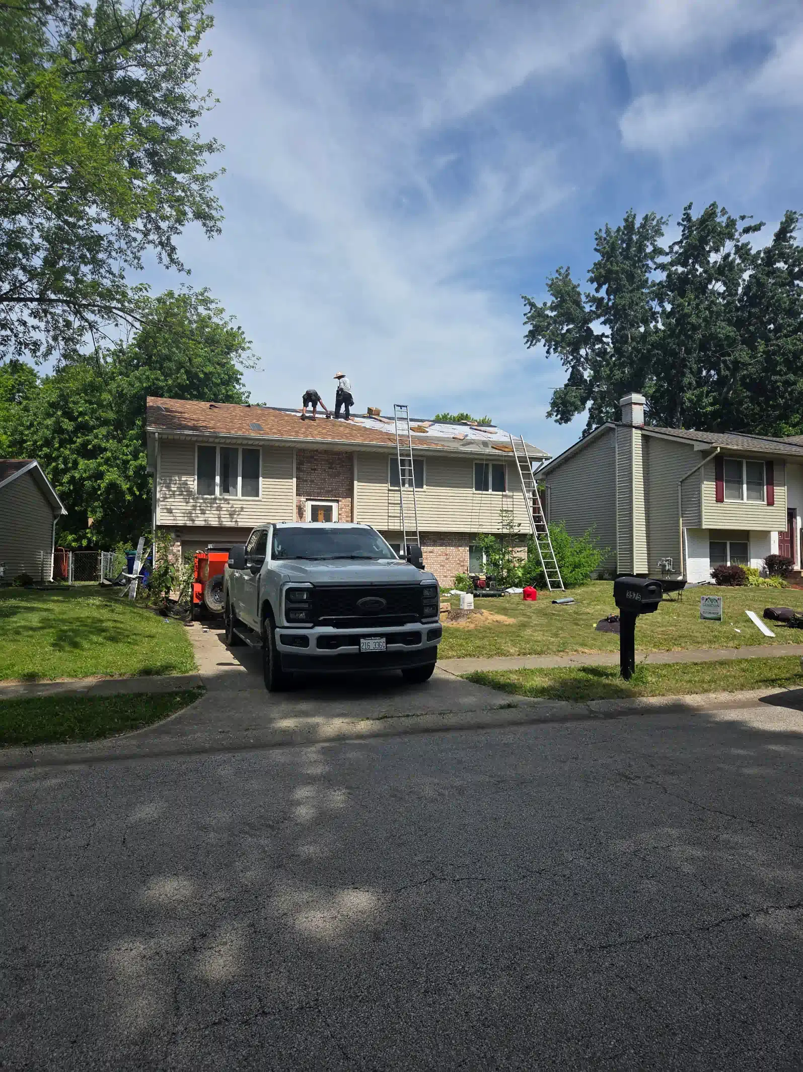 A white pickup truck parked in the driveway of a house undergoing roof repairs on a sunny day.