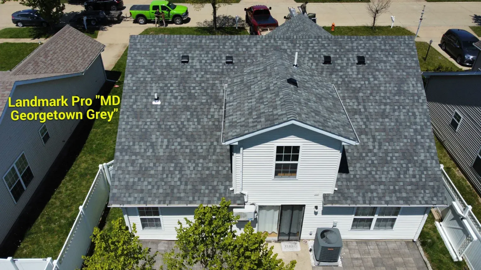 Aerial view of a white house with a new Landmark Pro Georgetown Grey shingled roof, surrounded by neighboring homes.