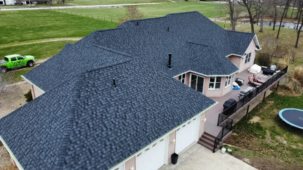 Aerial view of a house with a dark gray shingled roof, a back deck, and a green truck parked on the side.