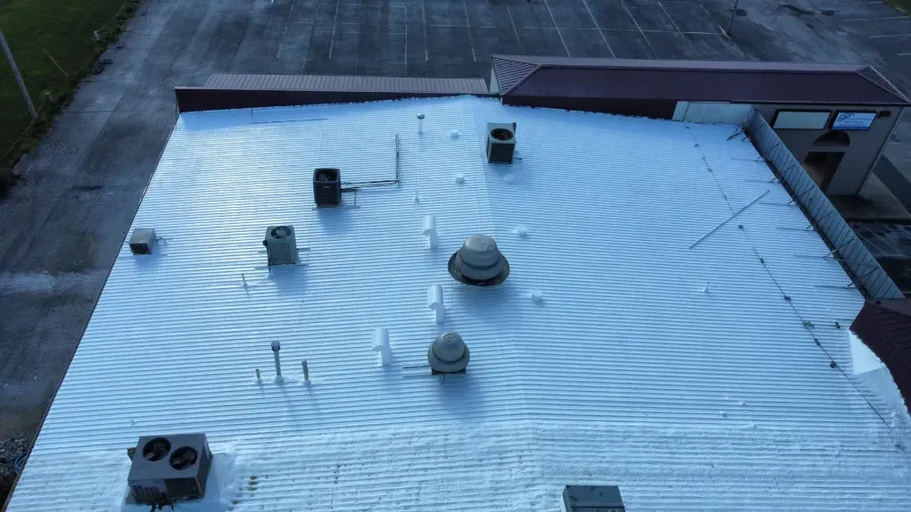 Aerial view of a white, textured roof featuring repeating, ripple-like patterns caused by sunlight and shadows.
