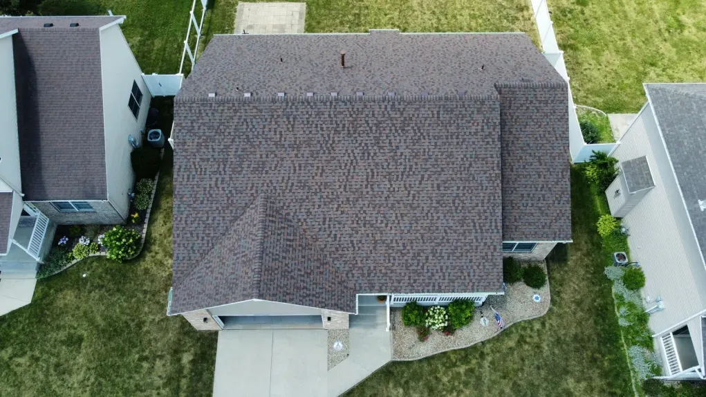 Aerial view of a residential suburban home with a dark shingled roof, a paved driveway, and surrounding lawn.