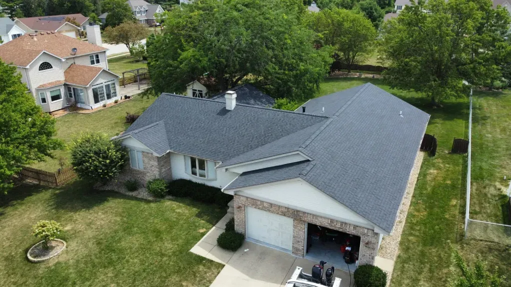 An aerial view of a single-story suburban home with a dark gray shingled roof, stone accents, and a two-car garage.
