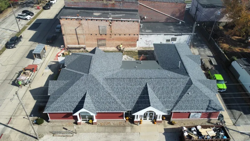 Aerial view of a red-brick commercial building with a dark grey shingled roof, located on a city street.