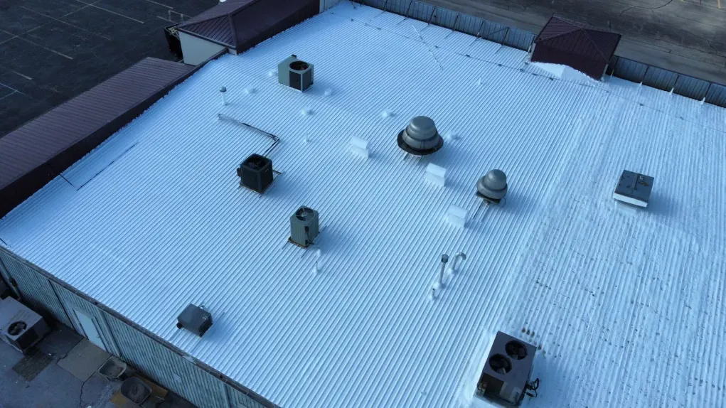 An aerial view of a flat building roof with a white membrane coating, featuring multiple HVAC units and exhaust vents.