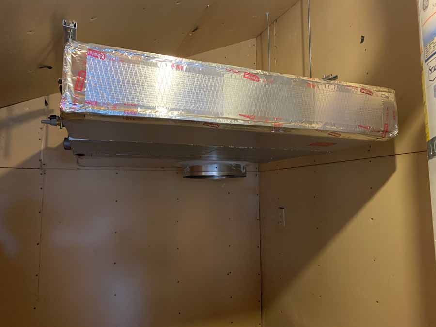 Metal ductwork and a ceiling-mounted vent inside an unfinished room with brown walls