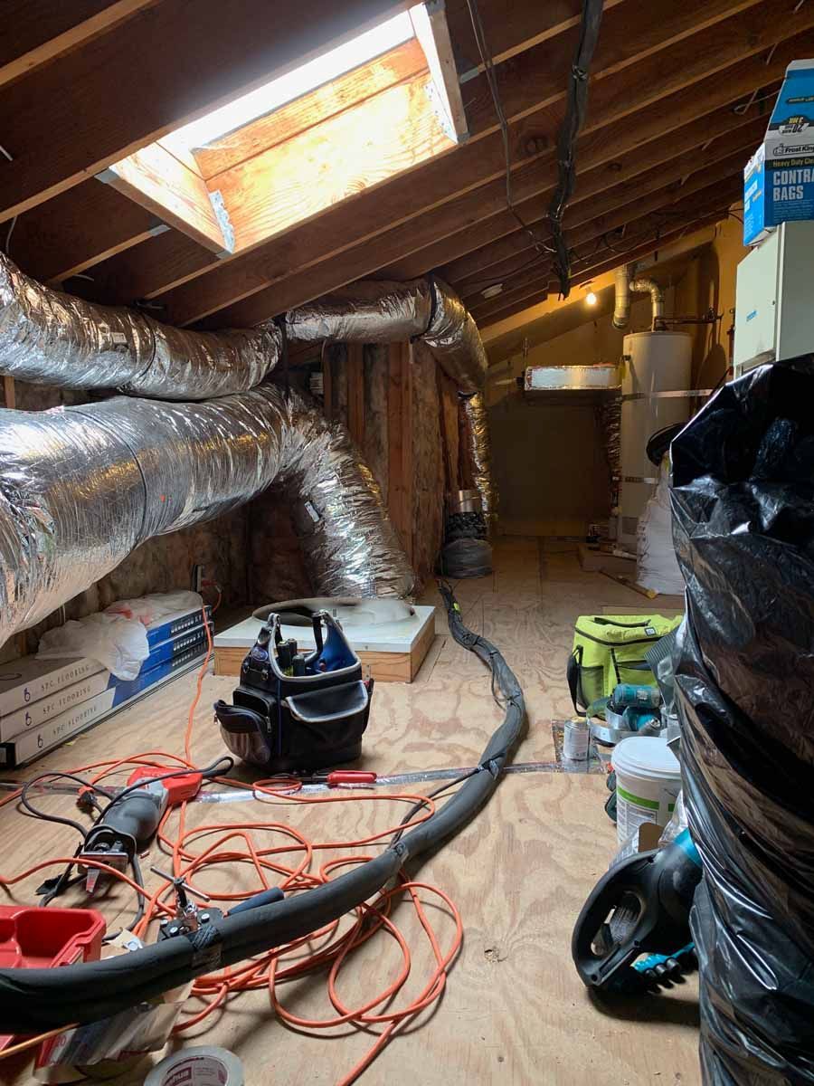 Unfinished attic with exposed insulation, ducts, skylights, and tools, including a vacuum and cords on the floor