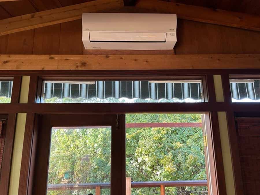 White wall-mounted air conditioner above wooden-framed windows in a cabin interior