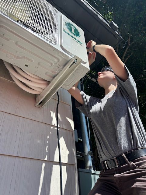 Technician working on an outdoor air conditioning unit mounted on a building wall