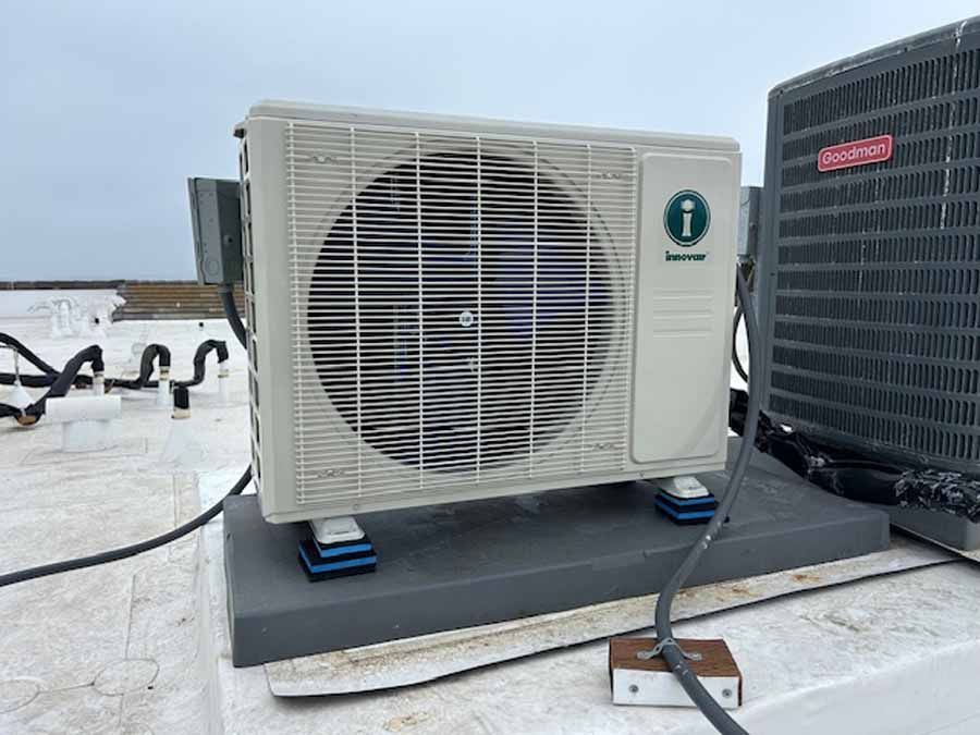 White rooftop HVAC unit on blue pads beside a larger black unit.