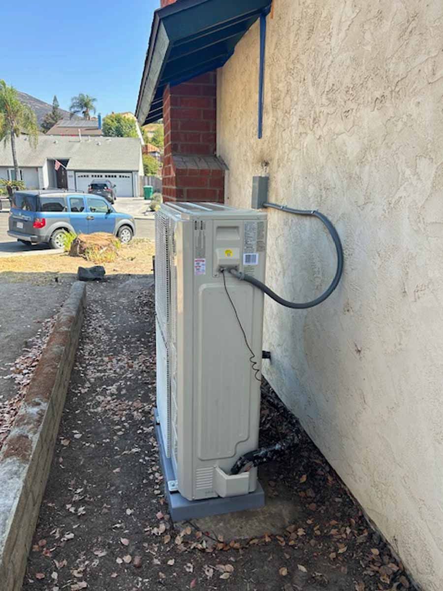 Outdoor electrical meter and utility box mounted beside a beige house wall, with a parked car in the background