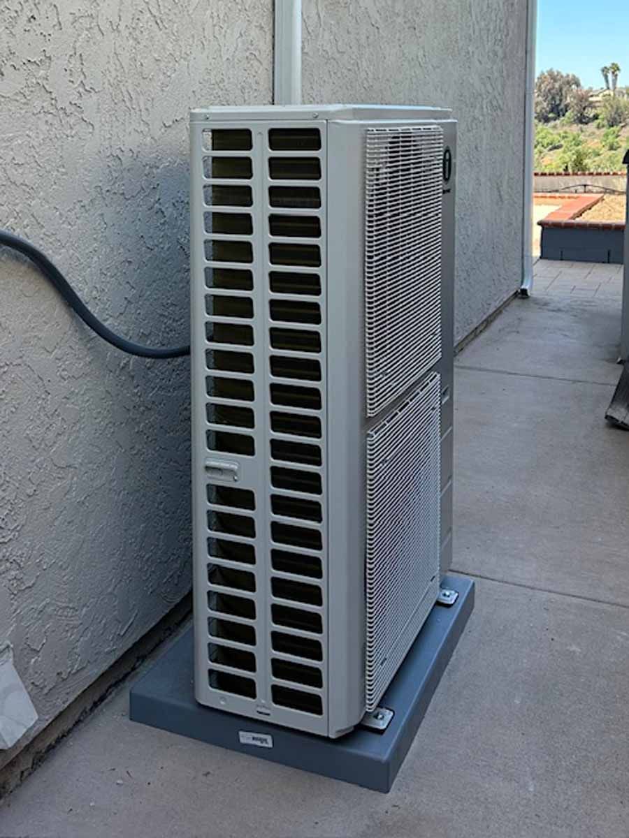 Outdoor HVAC unit on a concrete pad beside a stucco wall, with a hose attached.