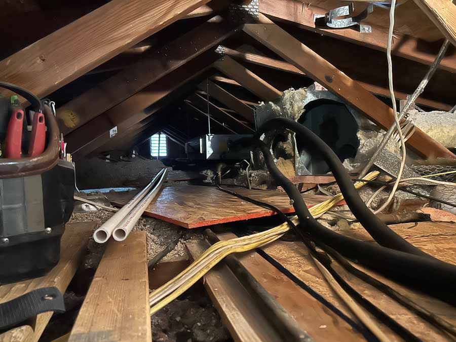 Attic crawlspace with exposed beams, cables, and tools scattered on the floorboards