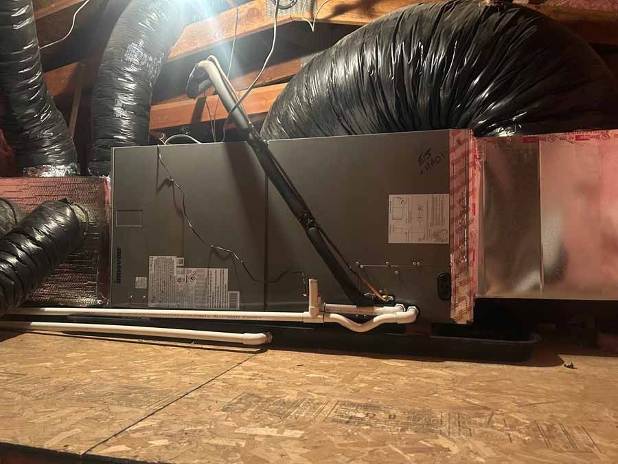 HVAC unit with exposed black ducting in an attic space, viewed from floor level.