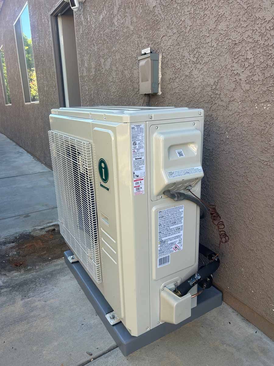 Beige outdoor air conditioning unit beside a stucco wall on a sidewalk.