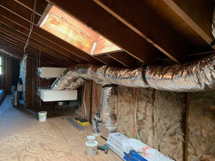 Attic with insulated ducts, exposed beams, and HVAC equipment under a sloped roof