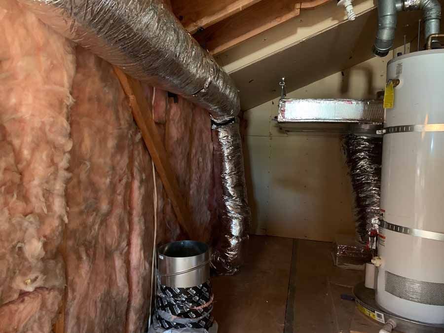 Insulated attic with ductwork, exposed rafters, and a water heater in a narrow service area