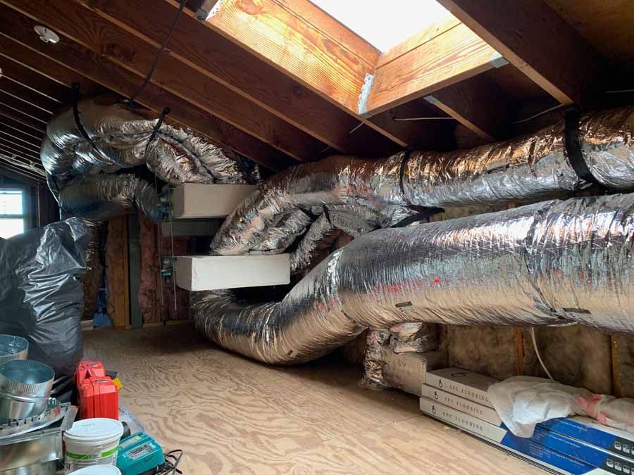 Attic crawlspace with insulated HVAC ducts, exposed beams, and storage items on the floor.