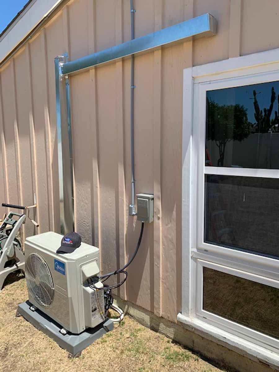 Outdoor HVAC unit mounted beside tan siding and a white-trimmed window with blue ductwork above.