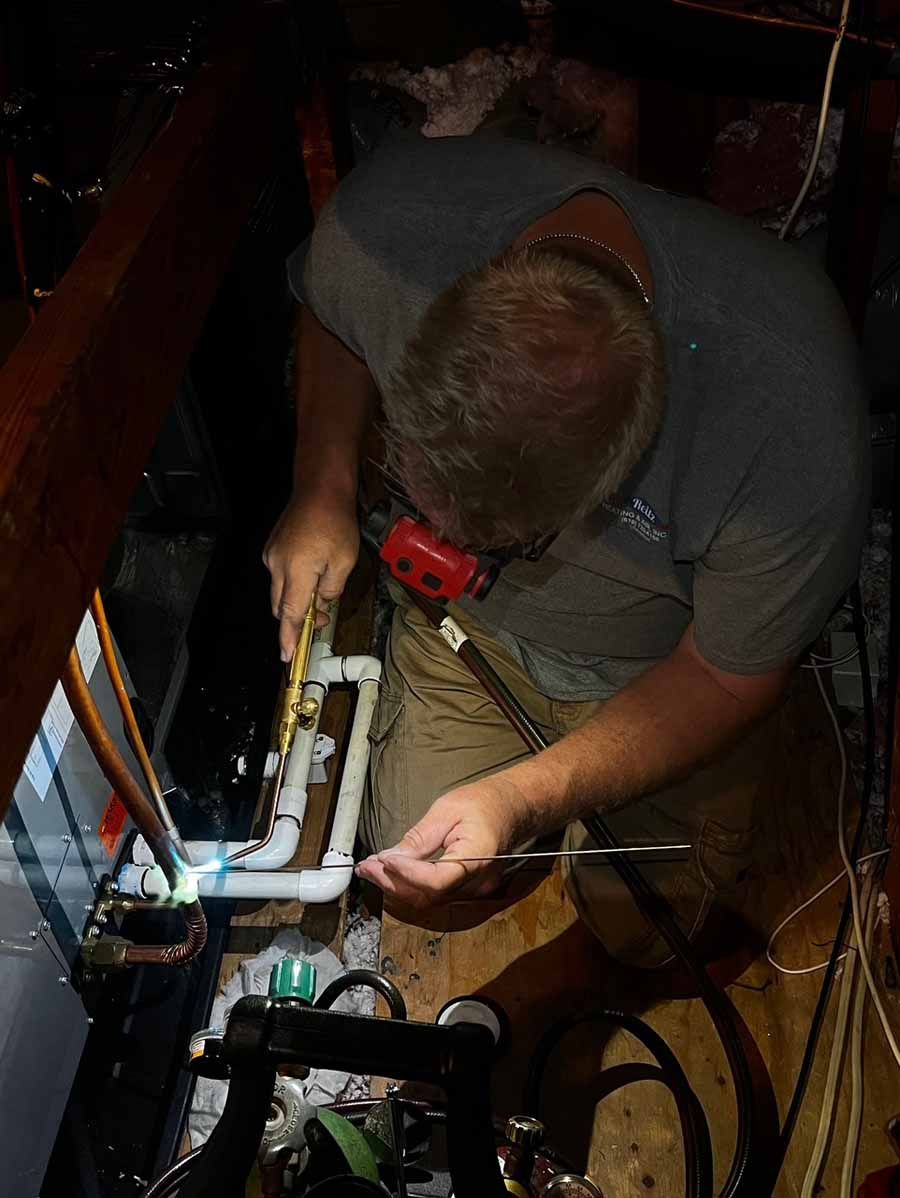 Technician working on a plumbing setup under a sink with tools and white PVC pipes.