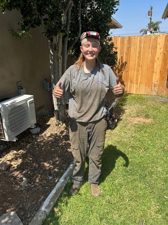 Person standing in a sunny backyard, smiling and giving thumbs up while holding a large fish.