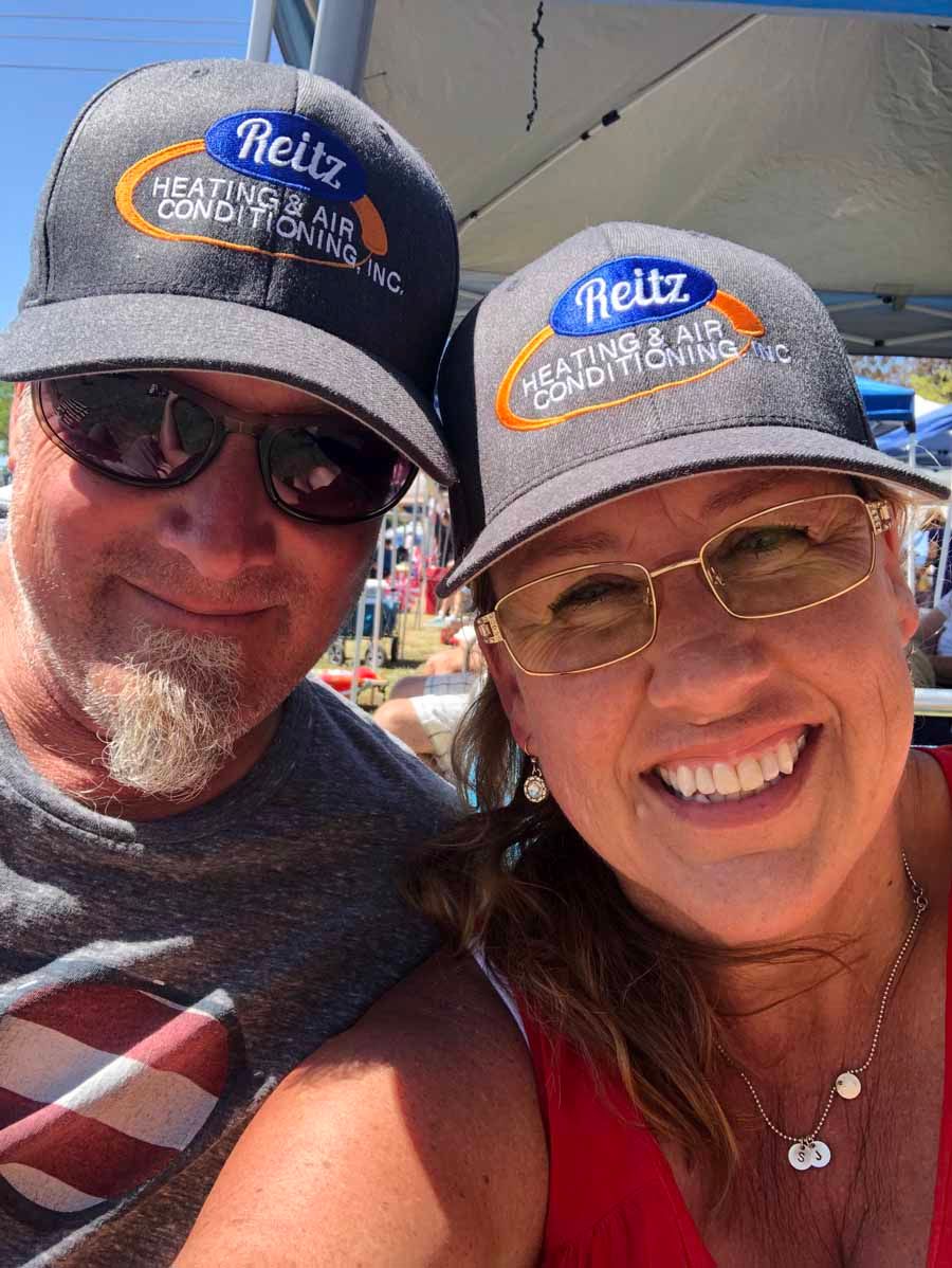 Two smiling people in matching Reitz caps and sunglasses taking a selfie outdoors